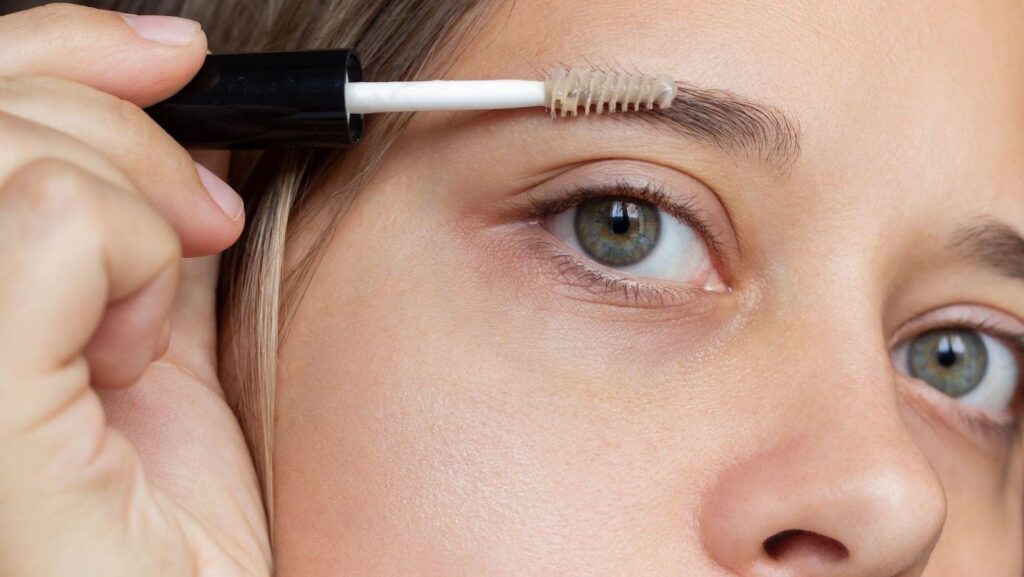 A young woman applying eyebrow care gel with a brush to support castor oil for eyebrows growth.