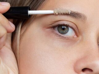 A young woman applying eyebrow care gel with a brush to support castor oil for eyebrows growth.