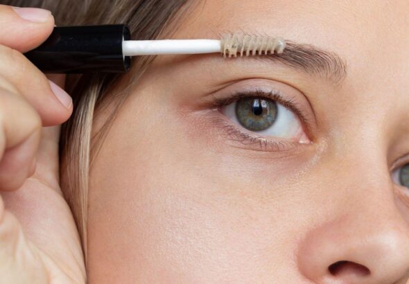 A young woman applying eyebrow care gel with a brush to support castor oil for eyebrows growth.