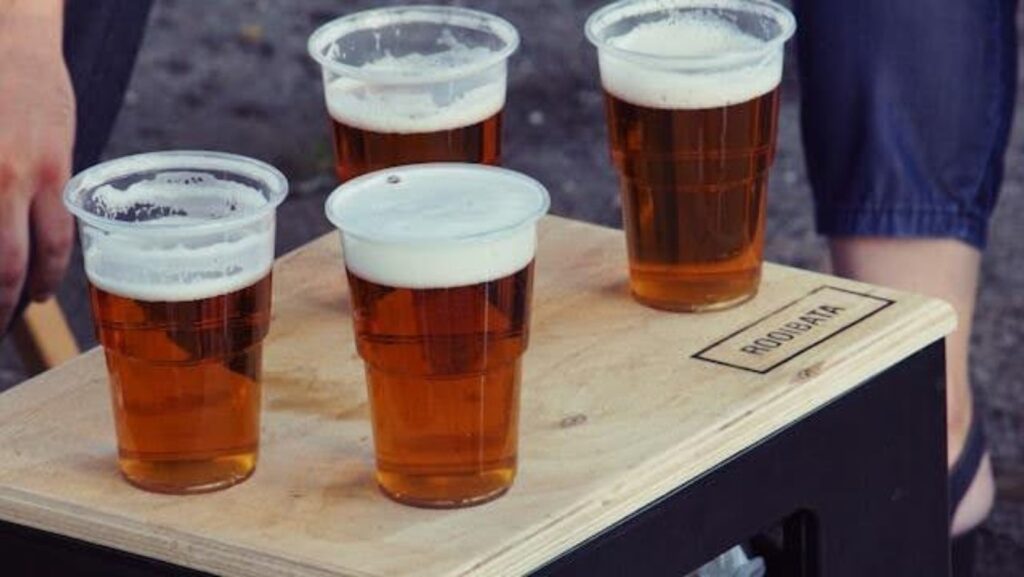 Four plastic glasses with beer, on a wooden table or chair.