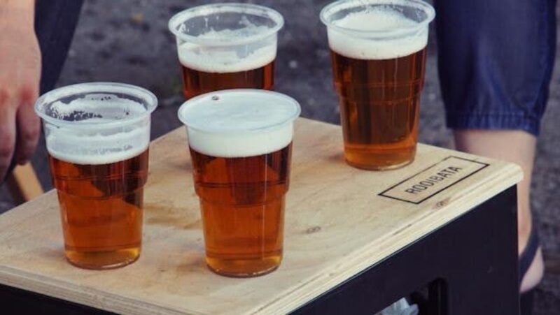 Four plastic glasses with beer, on a wooden table or chair.